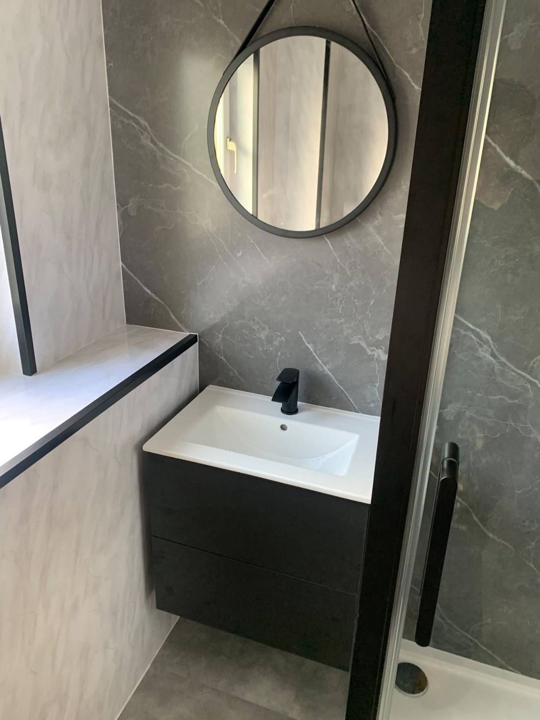 Wall-hung dark vanity unit with round mirror in a marble-effect bathroom